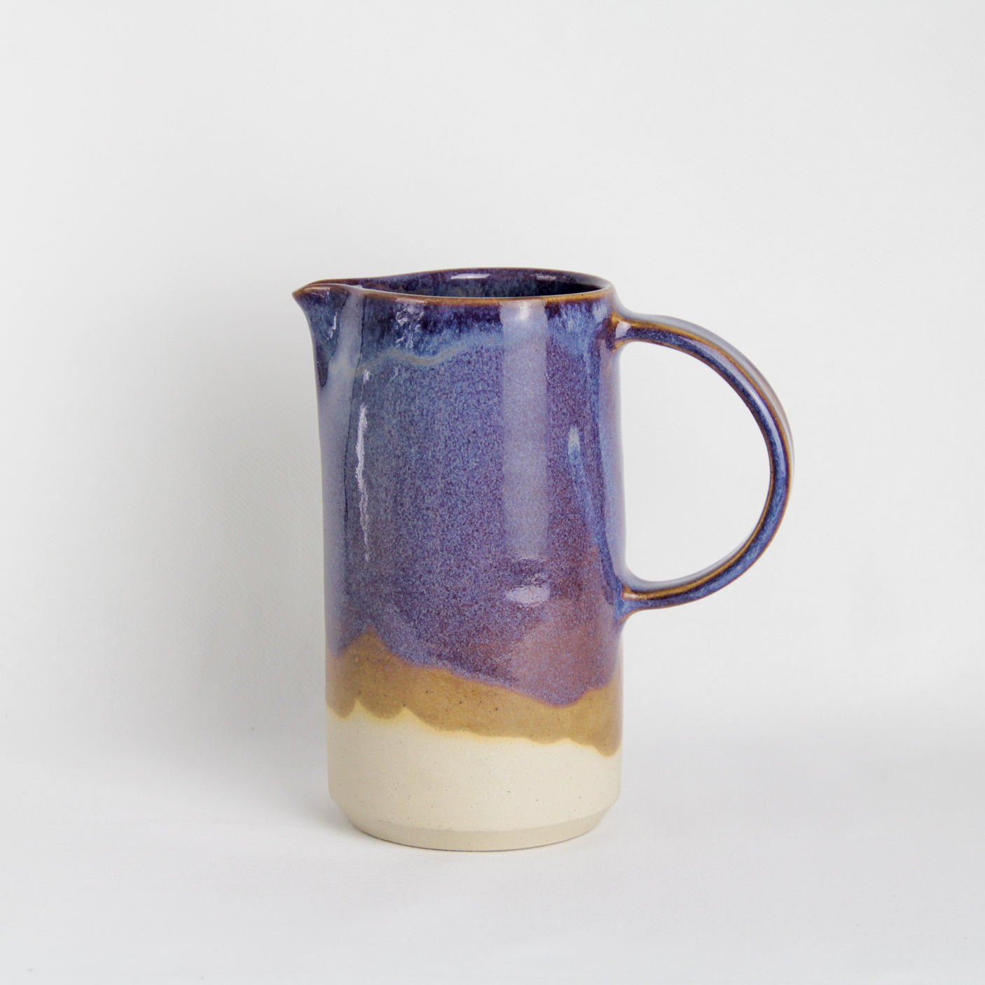 Image d'un pichet en céramique violet avec une grande anse sur fond blanc.