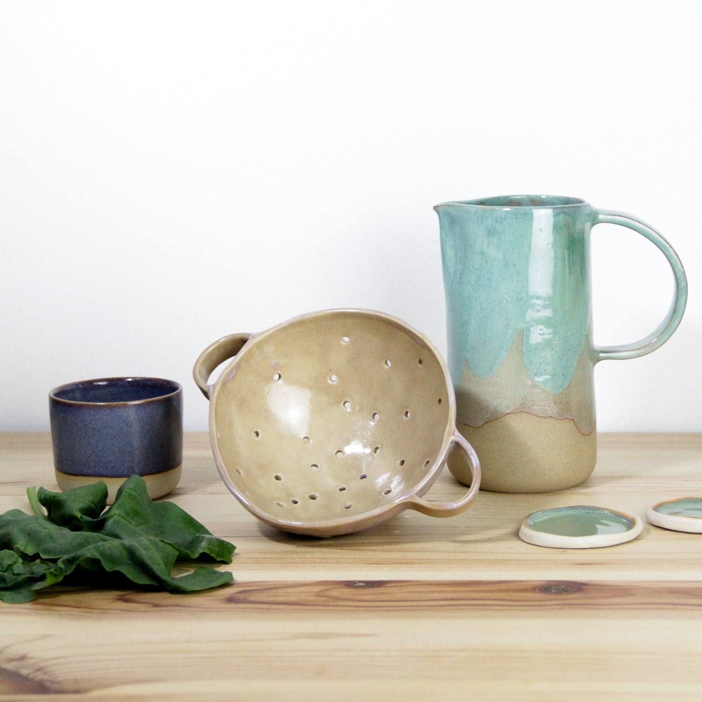 Image de plusieurs céramiques artisanales. On observe sur l'image un pichet céladon en grès, une passoire en céramique et une petite tasse violette.