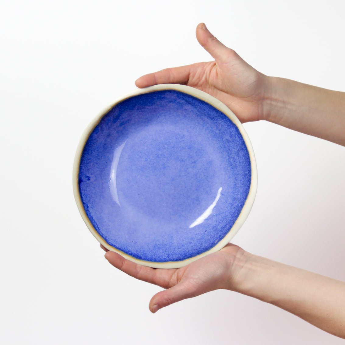 Image de deux mains qui tiennent une assiette creuse bleue roi pour présenter le produit