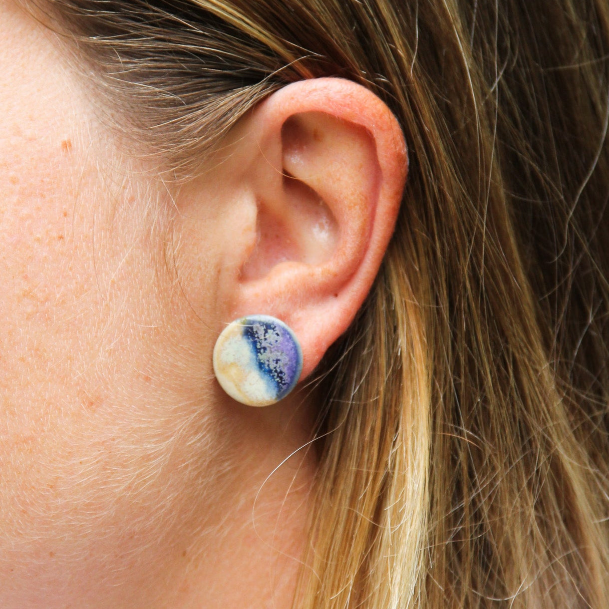 Image zoomée d'une femme qui porte une boucle d'oreille plate et ronde bicolore. La boucle d'oreille est en céramique