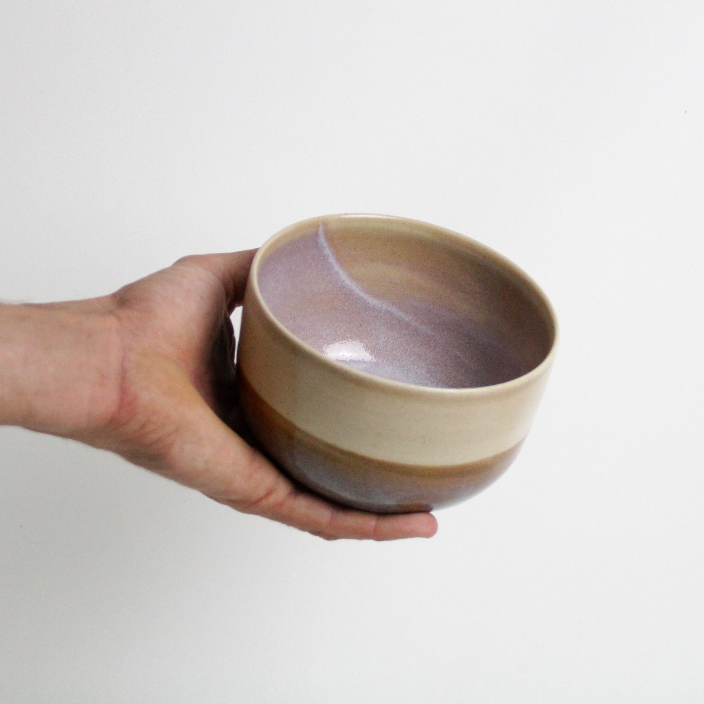 Photographie d'une main qui tient un bol en céramique bicolore issu
d'une fabrication artisanale