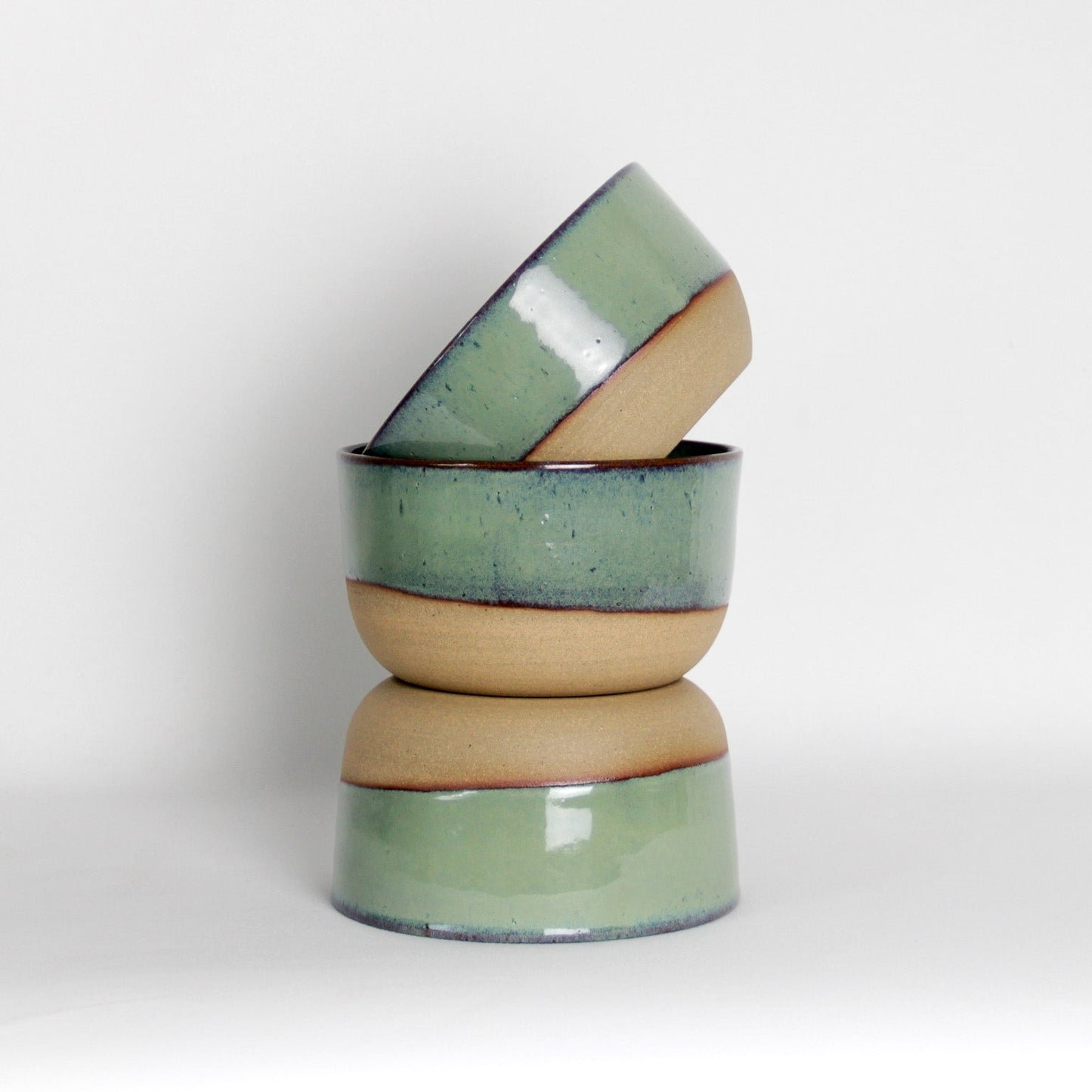 Image d'un ensemble de trois bols en céramique émaillé en vert. La partie basse de la pièce n'est pas émaillée pour un style moderne et unique.