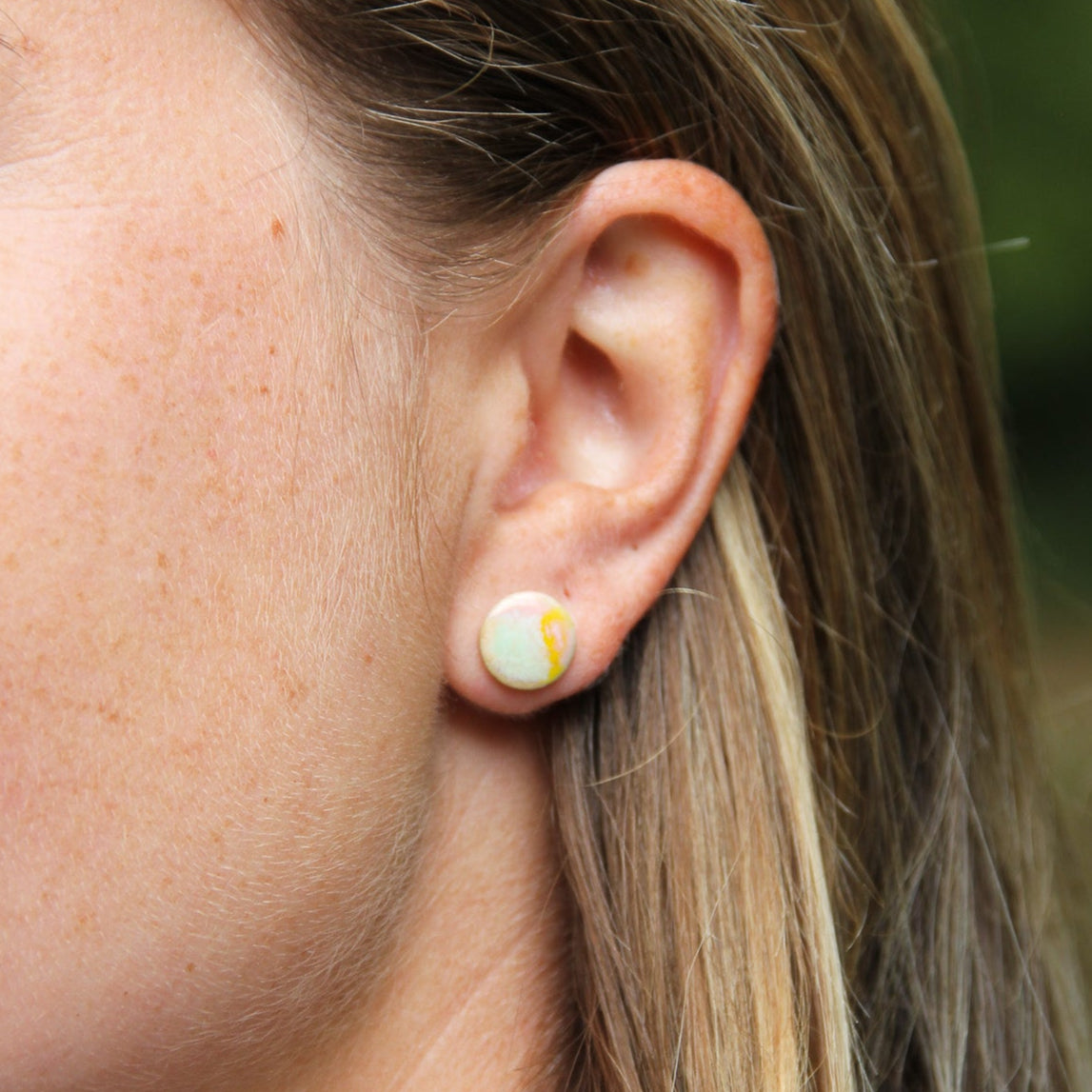 Image d'une boucle d'oreille portée par une femme. Petite puce d'oreille colorée et plate.