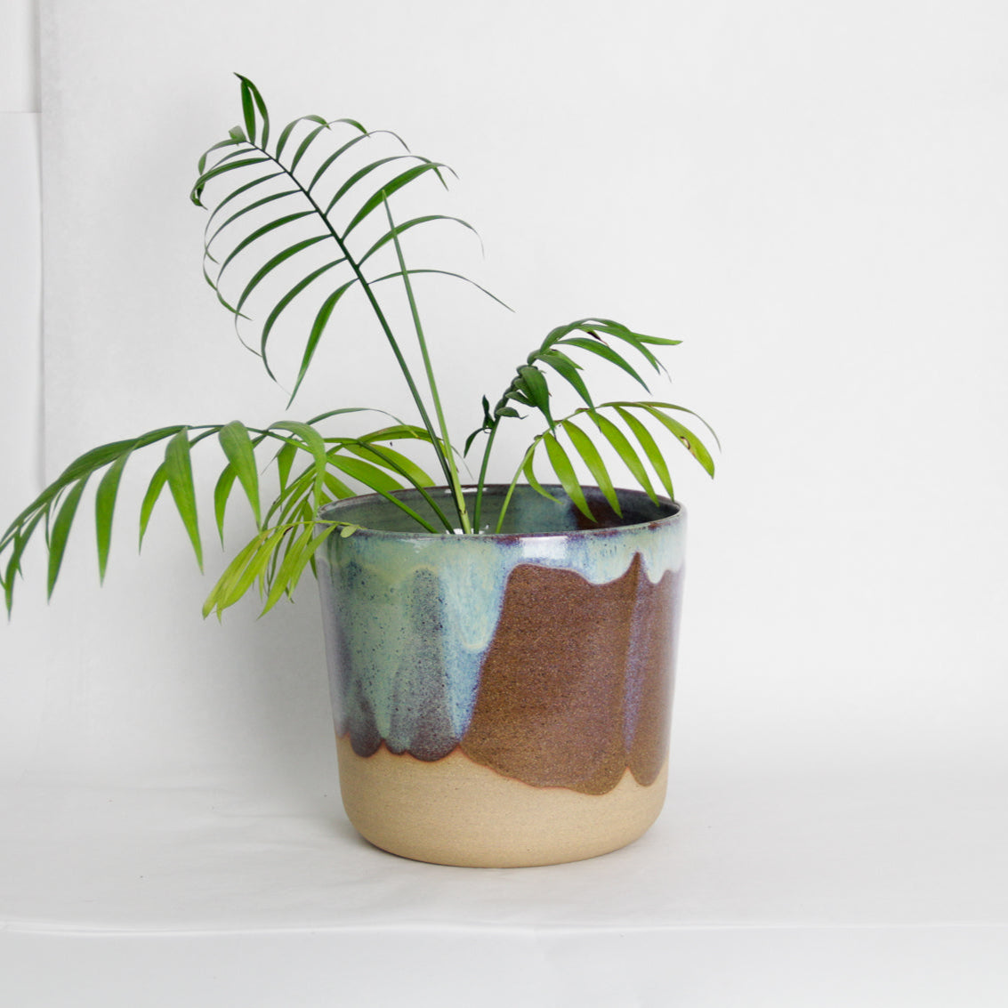Image d'un cache-pot en céramique artisanale. Le pot contient une plante verte. Le style du cache-pot est moderne et coloré.