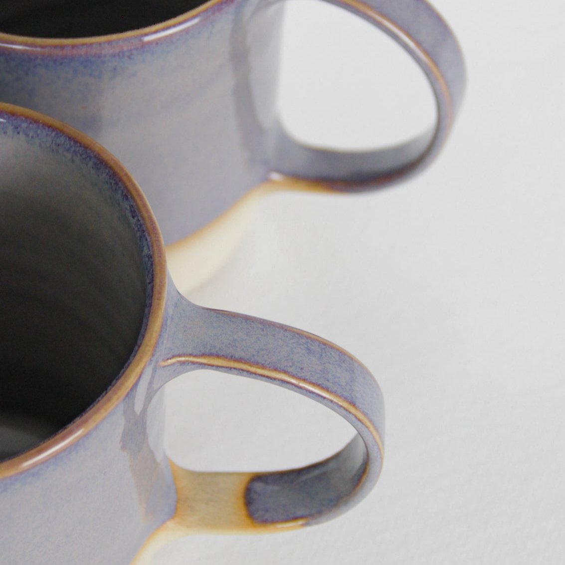 Image d'un détail de mug. On voit les anses qui ne sont pas émaillées de la même manière. L'une est complètement recouverte d'émail violet et l'autre non.