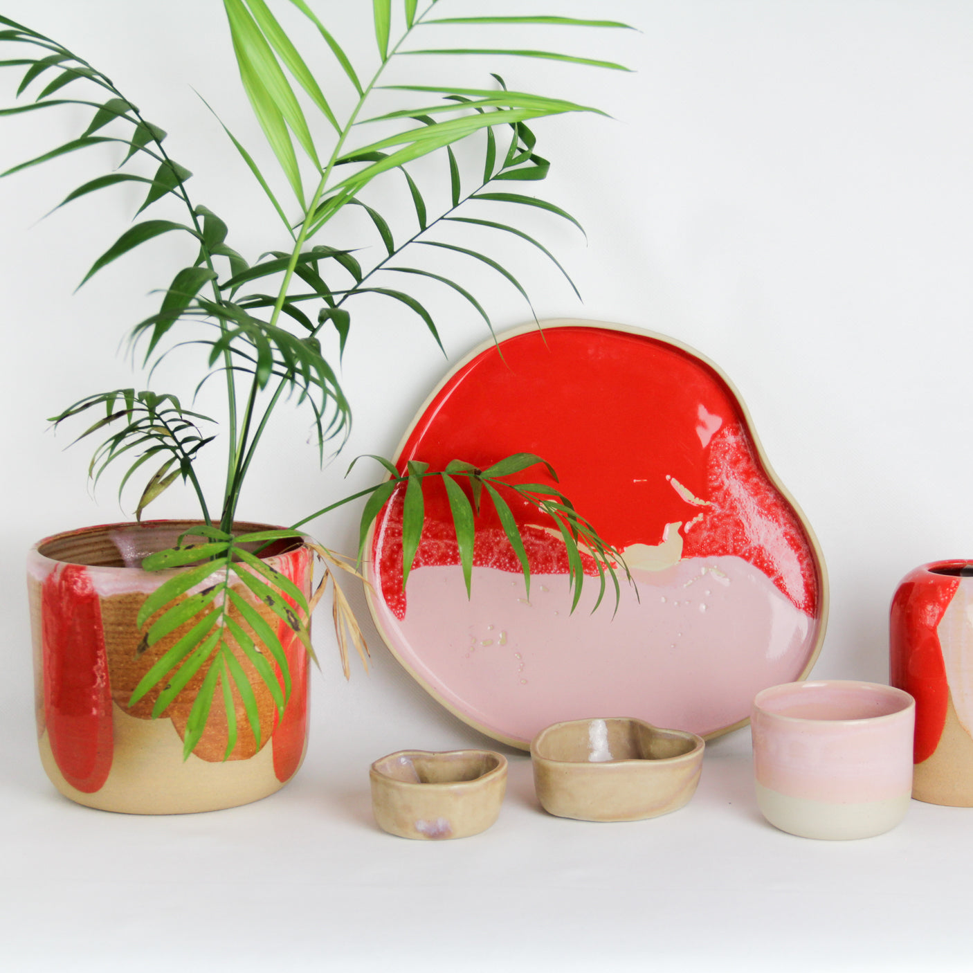 Image de plusieurs pièces en céramique aux couleurs roses et rouges. On voit un grand plateau à côté d'un cache-pot en grès.