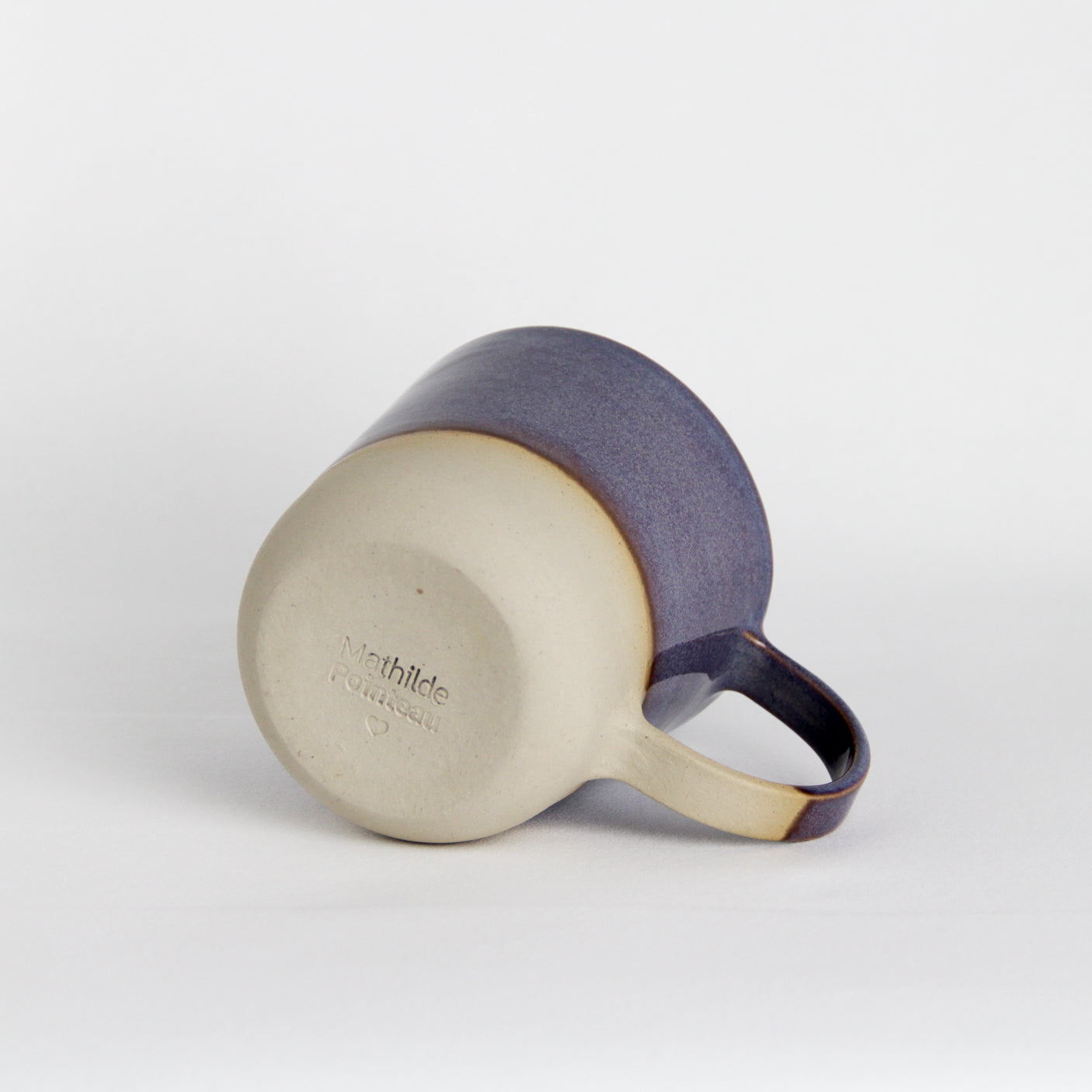 Image d'un mug en céramique vu de dessous. La partie basse de la pièce n'est pas émaillée et on peut sentir la texture de la terre.