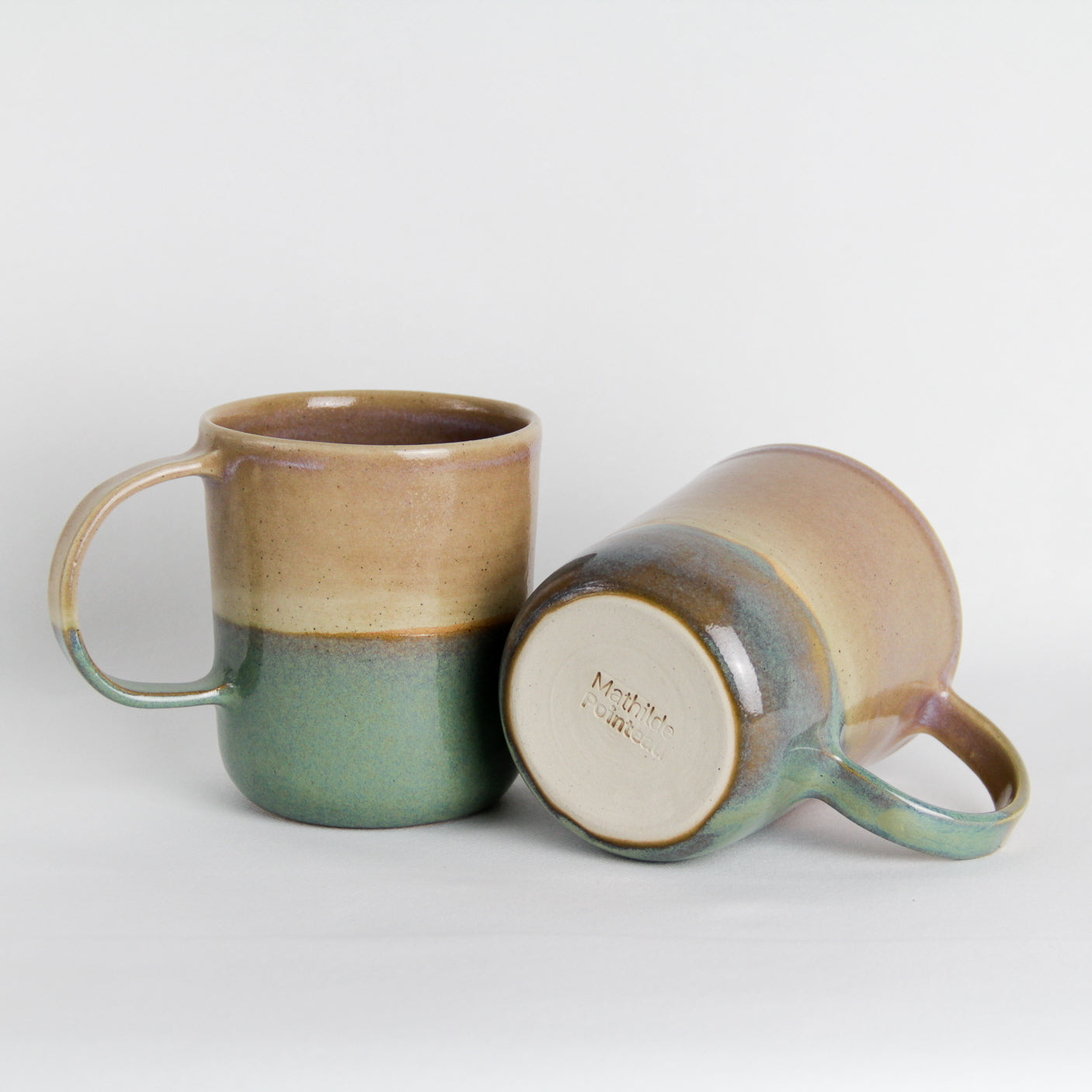 Image de deux mugs en céramique avec une grande anse. Ils sont bicolores rose et vert.