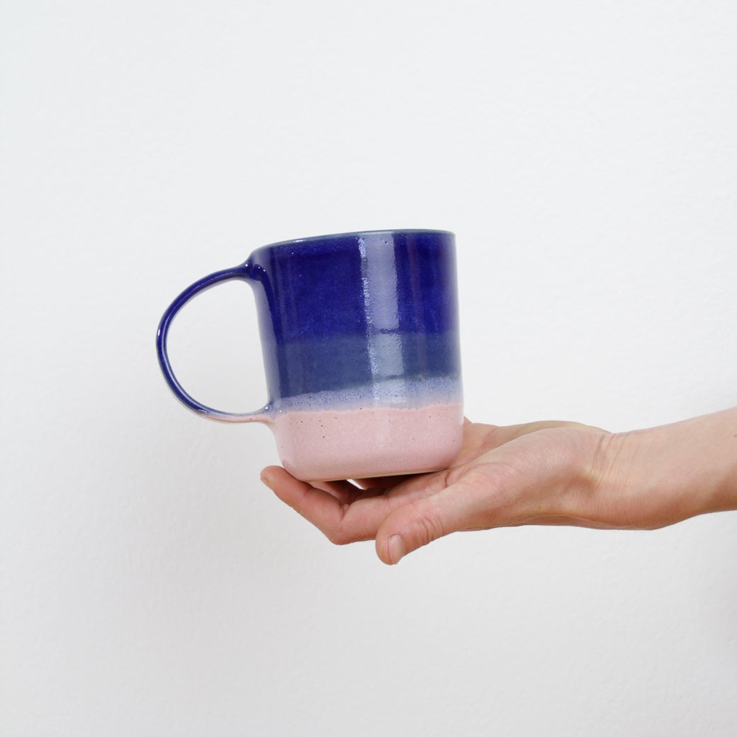 Image d'un mug rose et bleu en céramique artisanale présenté par une main tendue