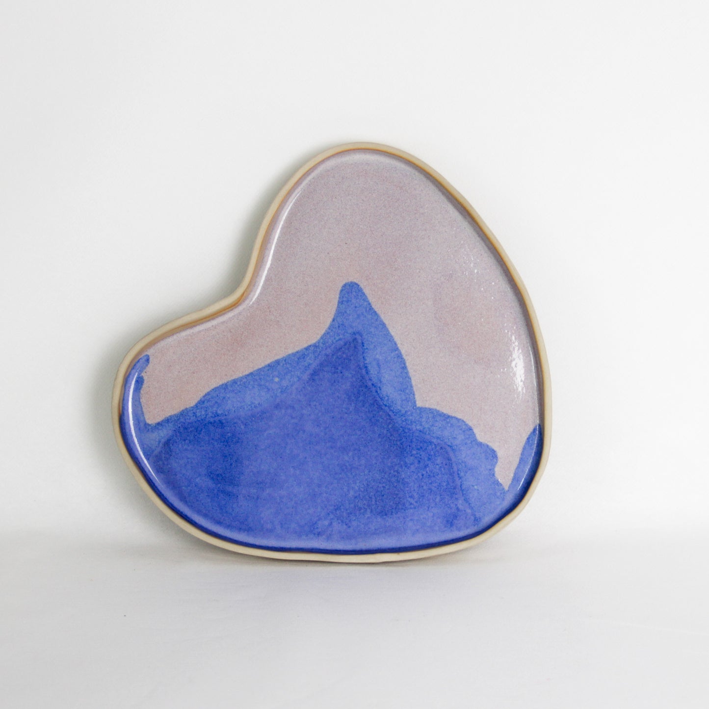 Image d'un plateau en céramique en forme de coeur. Le plateau est fabriqué à la main, il est bleu et rose. Il mesure environ 25 cm de diamètre.