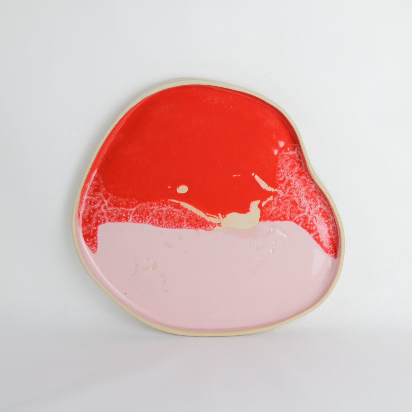 Image d'un plateau artisanal en céramique rose et rouge. Sa forme est aléatoire. Il mesure environ 27 cm de diamètre.