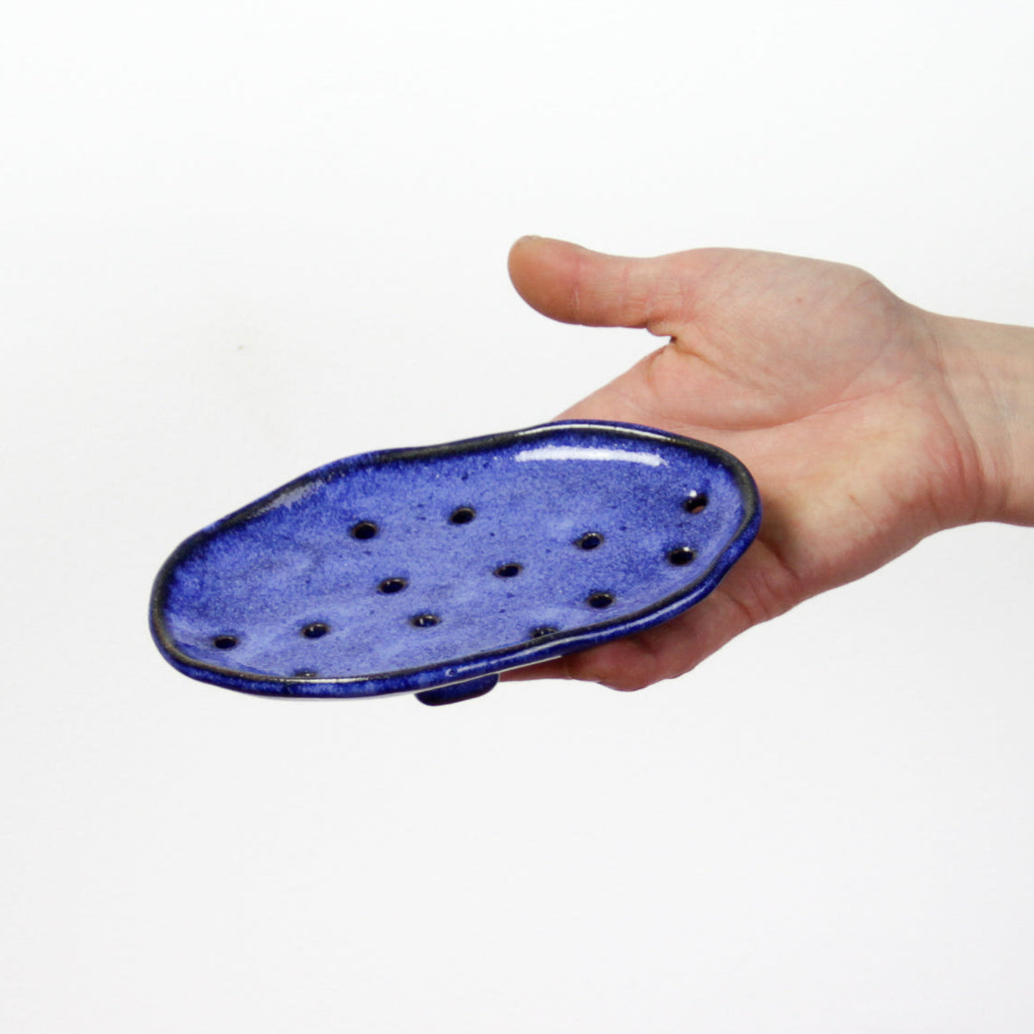 Image d'une main qui présente un porte-savon avec une forme organique et plusieurs trous pour laisser draine l'eau. Forme originale et belle couleur bleue.