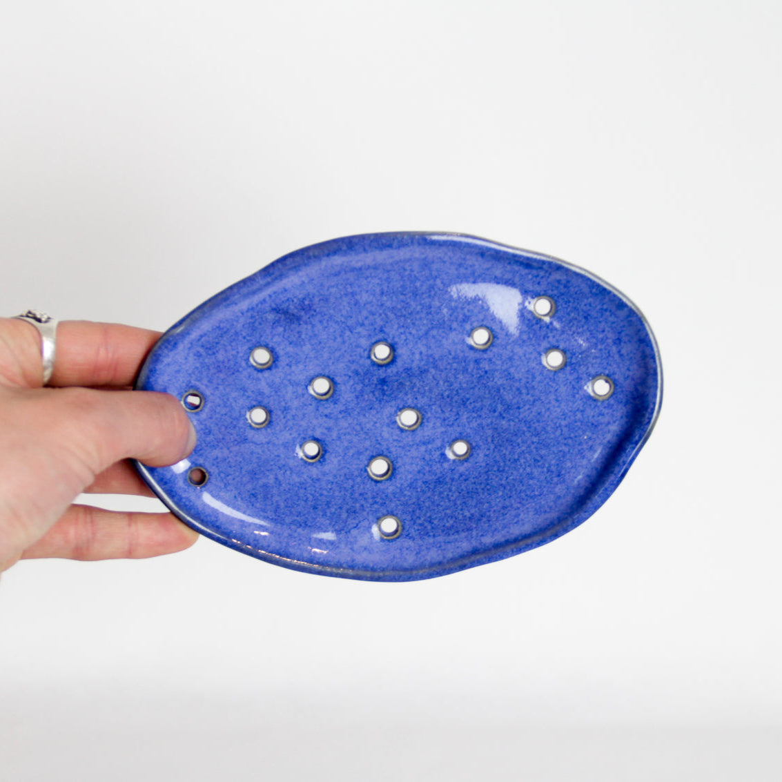 Image d'un porte-savon en céramique de couleur bleu de forme irrégulière. Beaucoup de trous pour laisser drainer l'eau.
