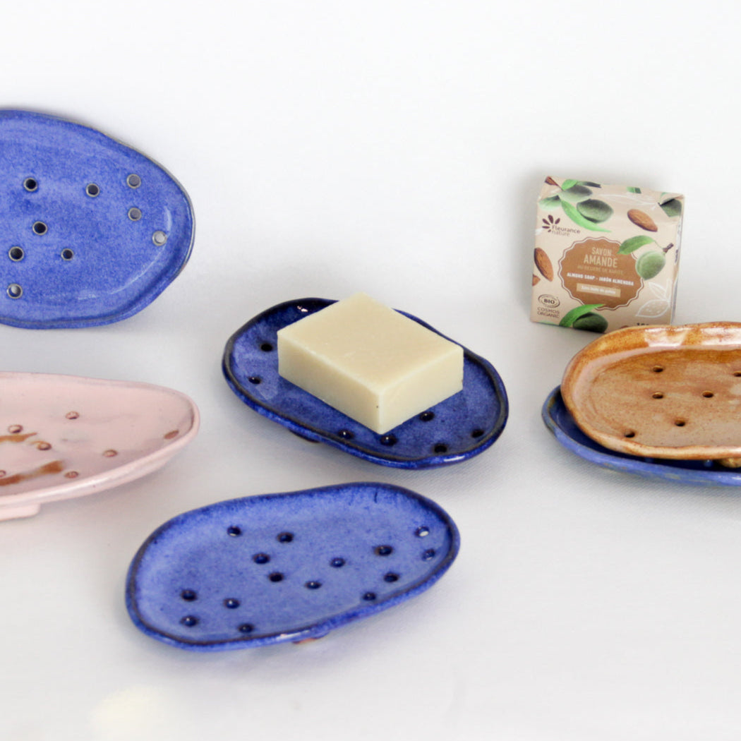 Image de plusieurs porte-savons de couleurs différentes. Forme aléatoire, beaucoup de petits trous pour laisser drainer l'eau. Ces supports à savon sont sur pieds. Produits design et original.