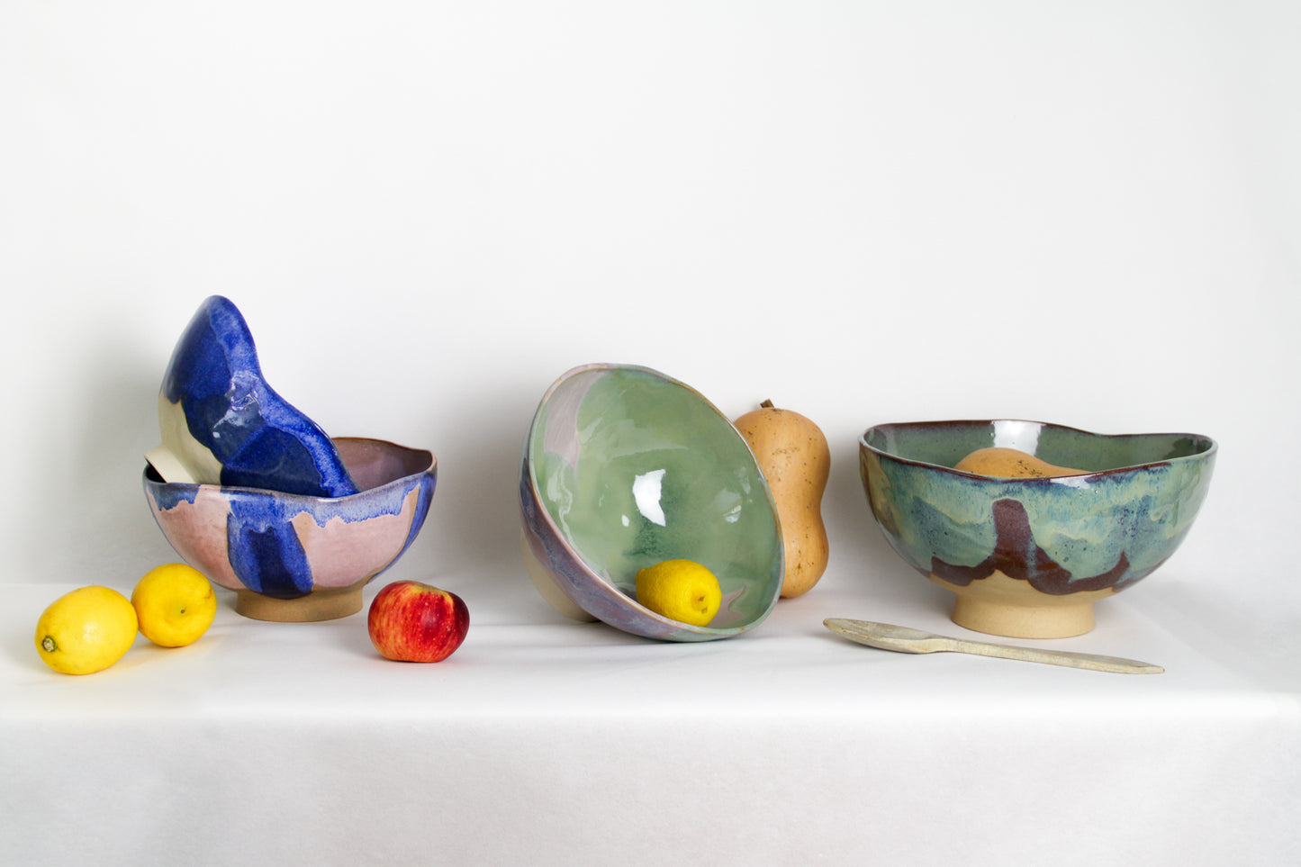 Image de quatre saladiers en céramique avec des fruits. On observe plusieurs tailles et plusieurs coloris. Les couleurs bleues, vertes et roses sont douces et intenses.