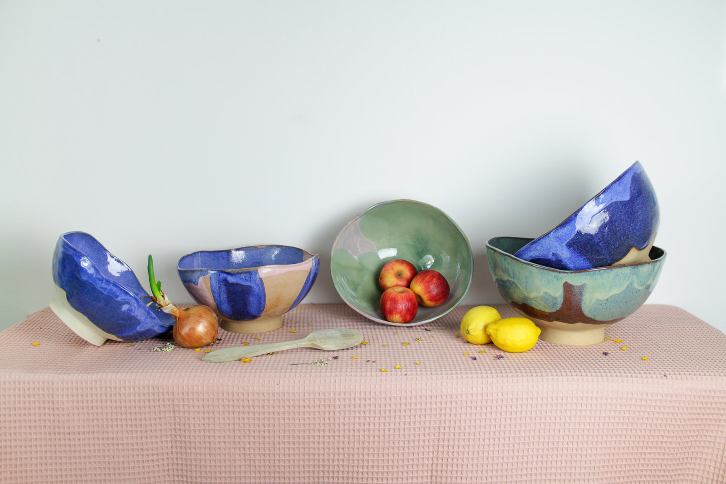 Image de cinq saladiers en céramique sur une nappe rose. C'est une présentation des tailles et des couleurs. Les saladiers sont colorés et irréguliers. Il y a du vert, du bleu et du rose.