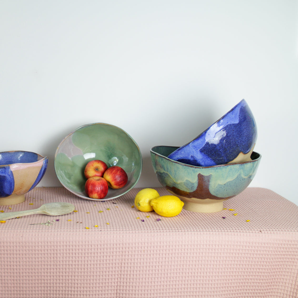 Image de cinq saladiers en céramique sur une nappe rose. C'est une présentation des tailles et des couleurs. Les saladiers sont colorés et irréguliers. Il y a du vert, du bleu et du rose.