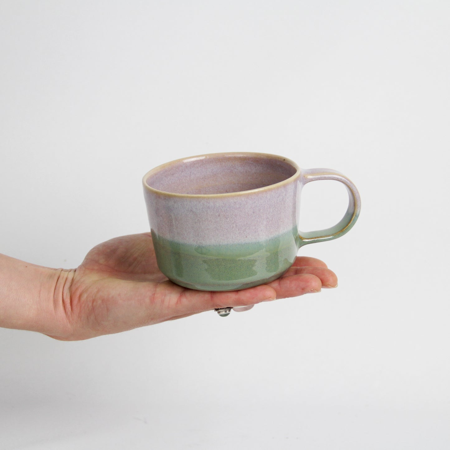 Image d'une main qui tient une petite tasse à café avec anse. Le céramique est bicolore rose et verte.