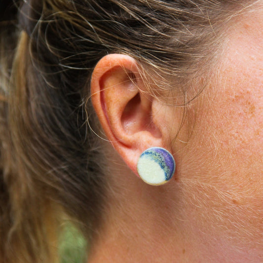 Image d'une boucle d'oreille en céramique de couleur menthe et violette portée par une femme. C'est une puce d'oreille ronde et plate.
