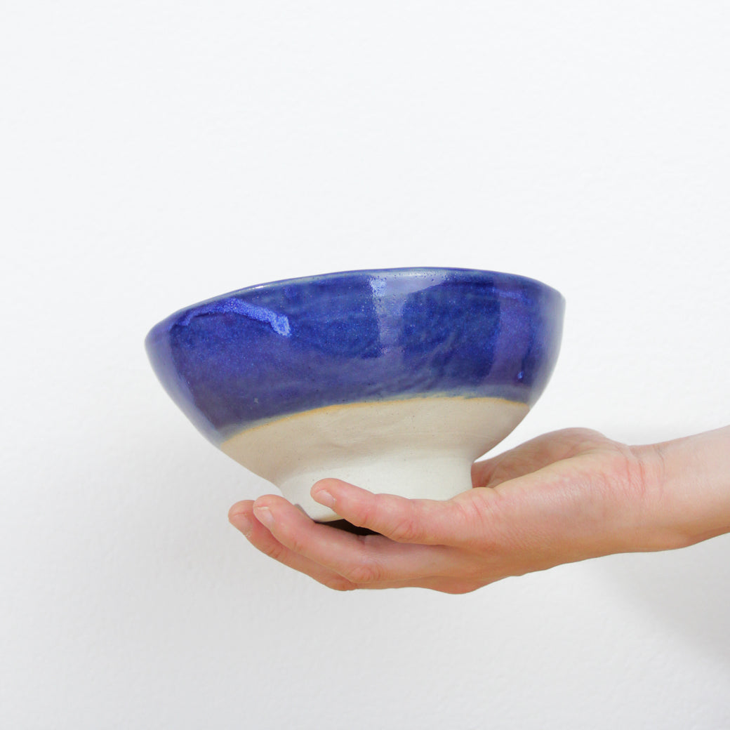 Image d'une main qui tient un bol à pied bleu en céramique artisanale faite en Bretagne