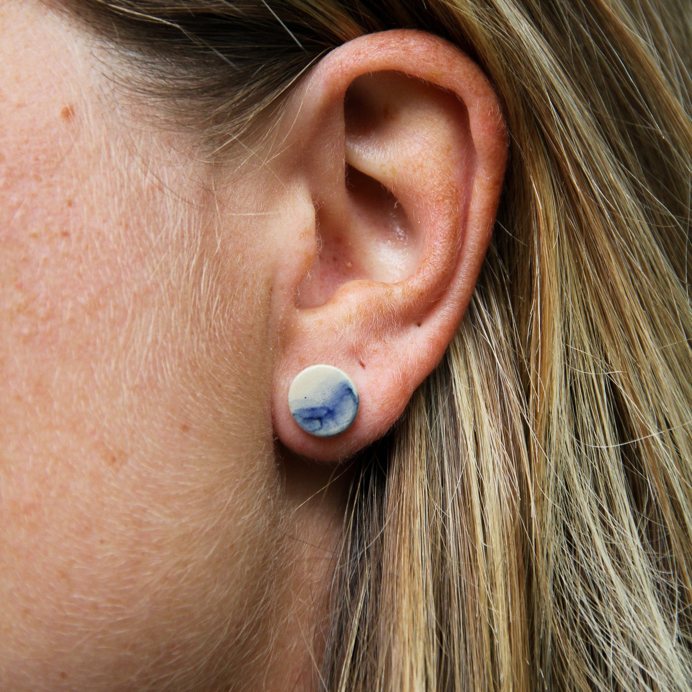 Image d'une femme qui porte une boucle d'oreille en céramique plate de la collection vague bleu.