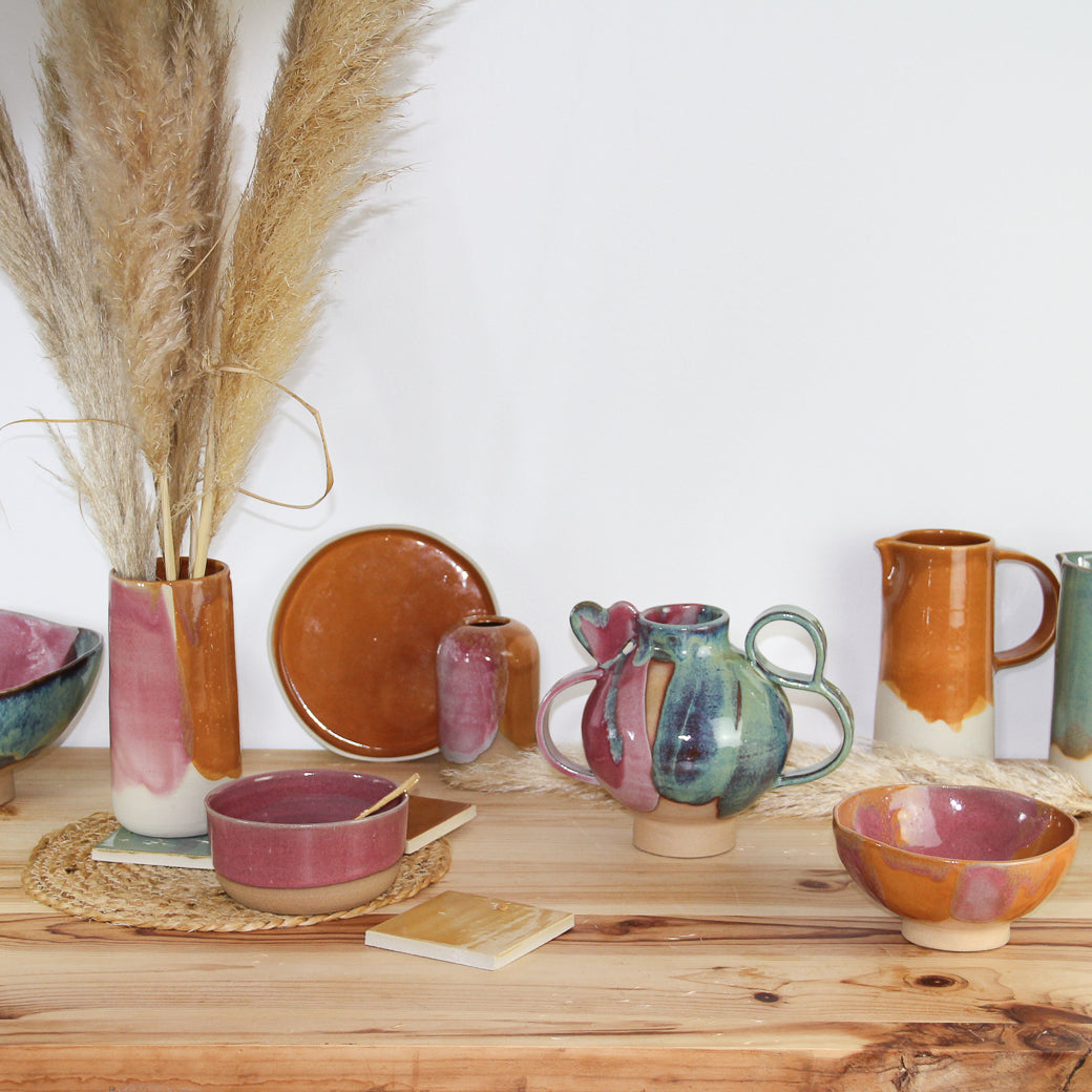 Photographie d'un ensemble de céramiques artisanales dans les tons de rose et caramel.  On voit des vases, bols, assiette et pichet.
