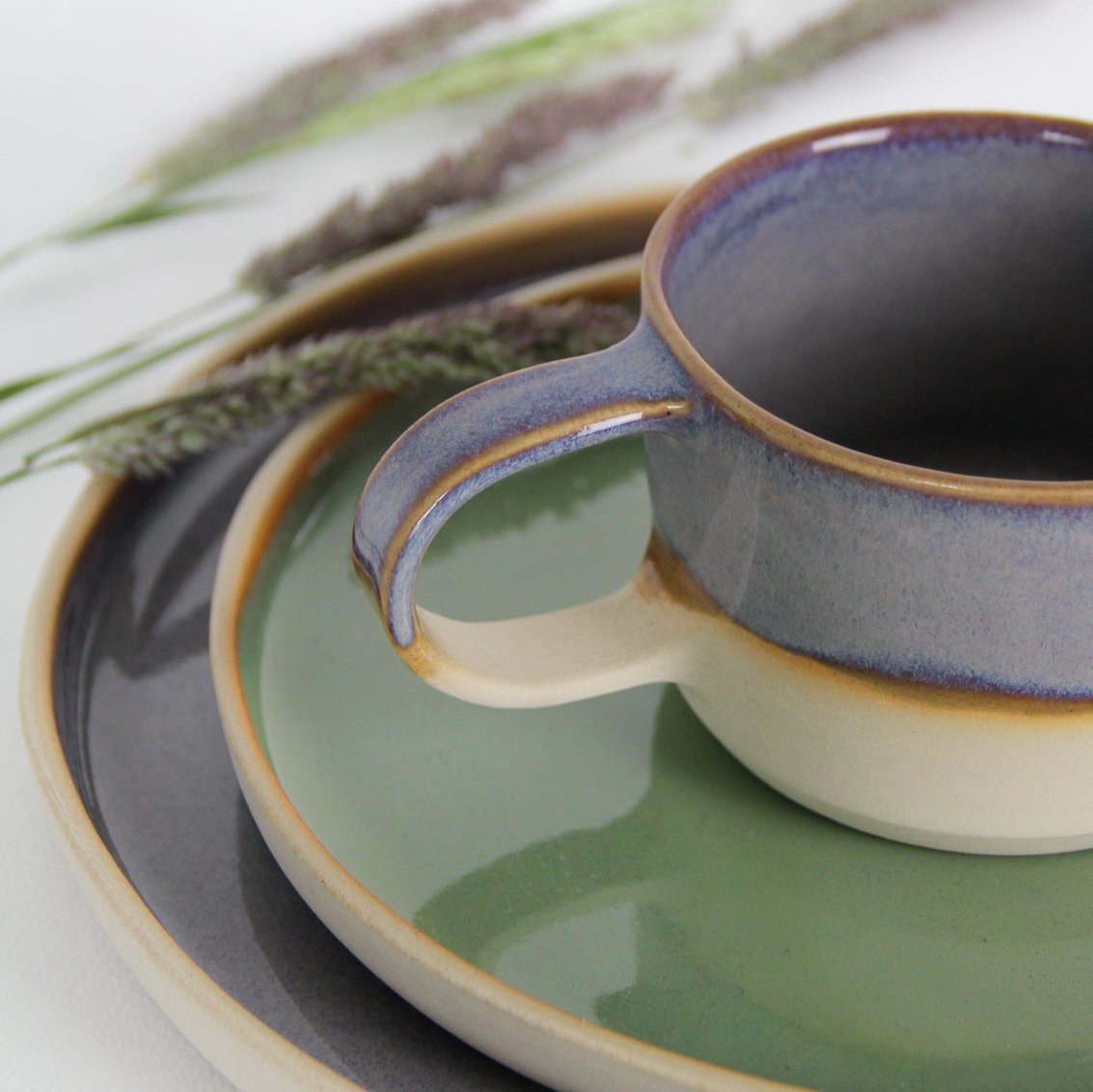 Image d'un détail de anse d'une tasse violette posée dans une assiette de couleur verte.