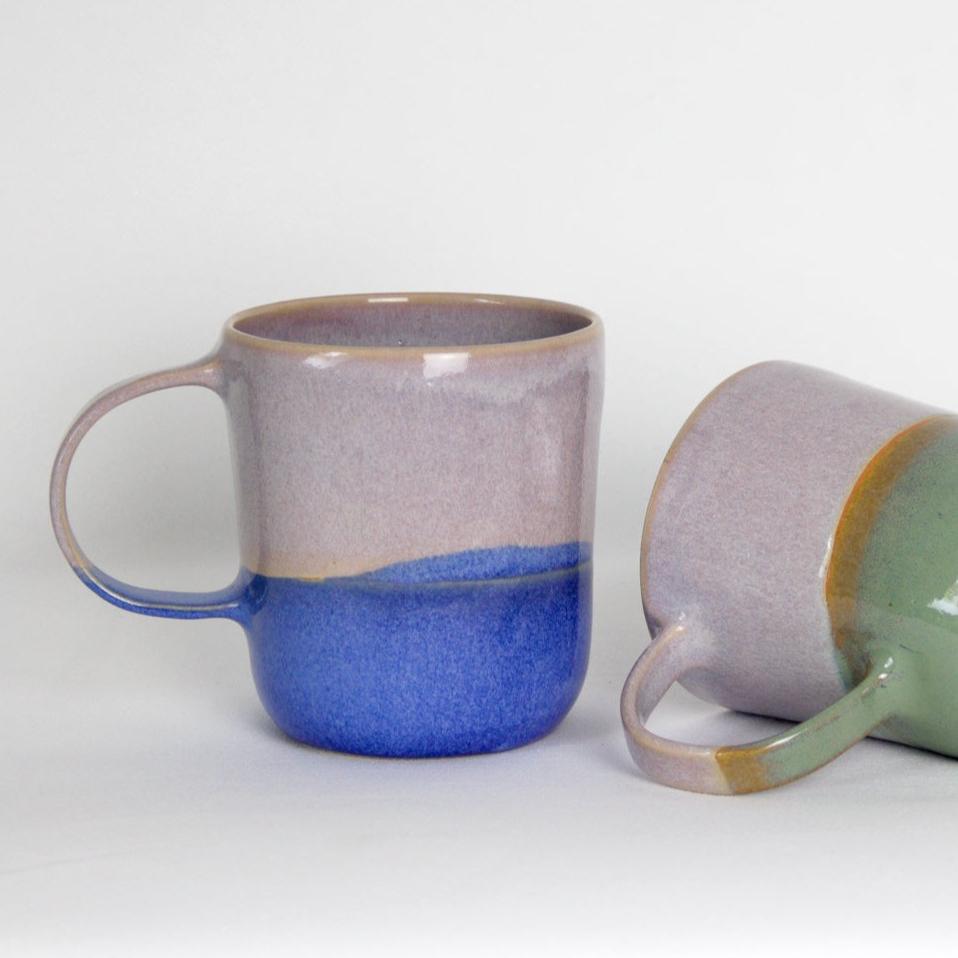 Image de deux mugs en céramique colorés et bicolores. Le premier est rose et bleu et le second est rose et vert. L'anse est grande.