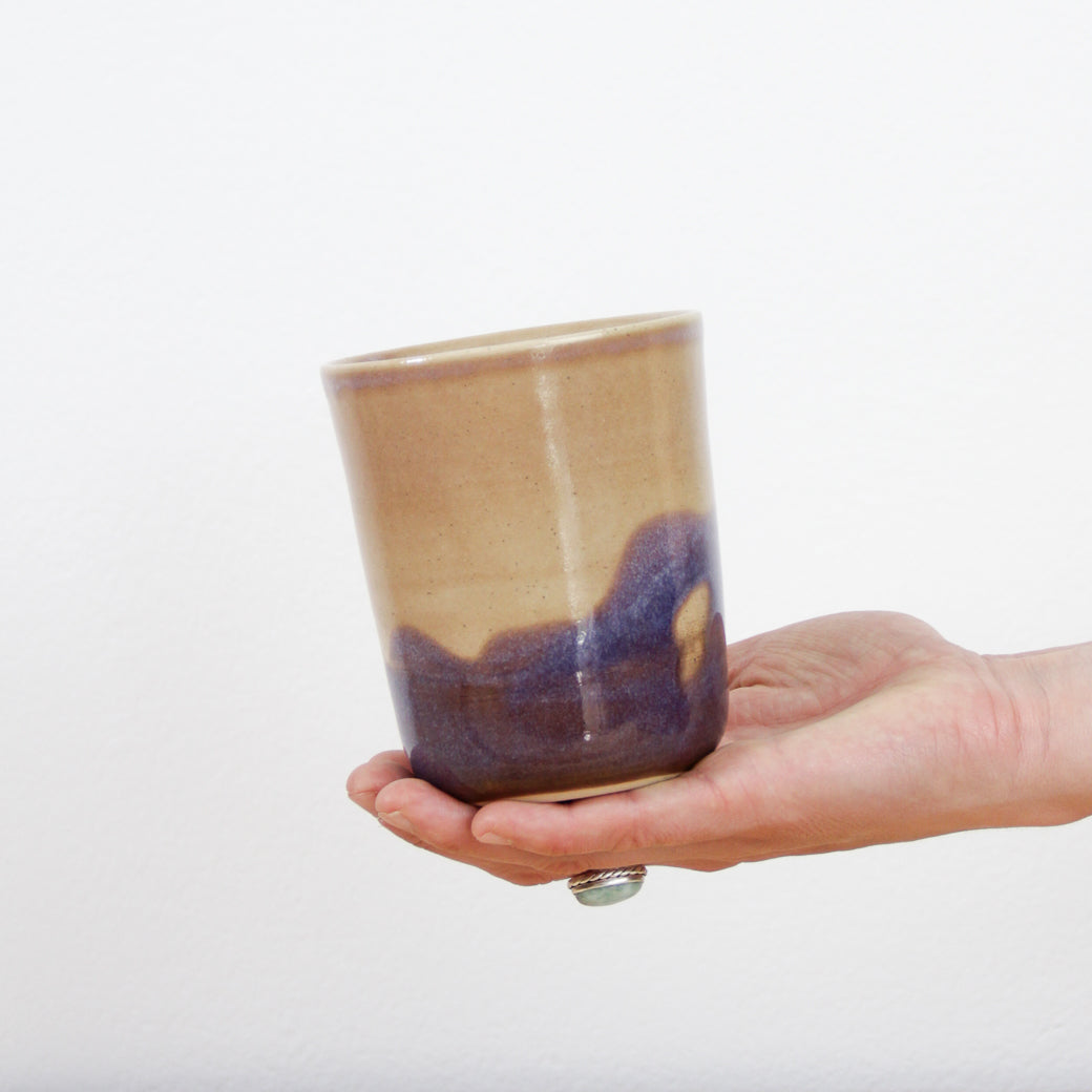 Image d'une main qui tient une grande tasse de type gobelet en céramique artisanale