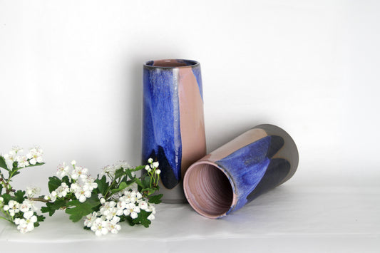 Image de deux vases bicolores rose et bleu. L'un des vases est couché. La forme volcanique apporte une touche moderne à l'objet. Les vases sont colorés.