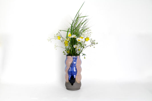 Image d'un grand vase en grès foncé avec un bouquet de fleur. Le vase est bicolore, rose et bleu. 