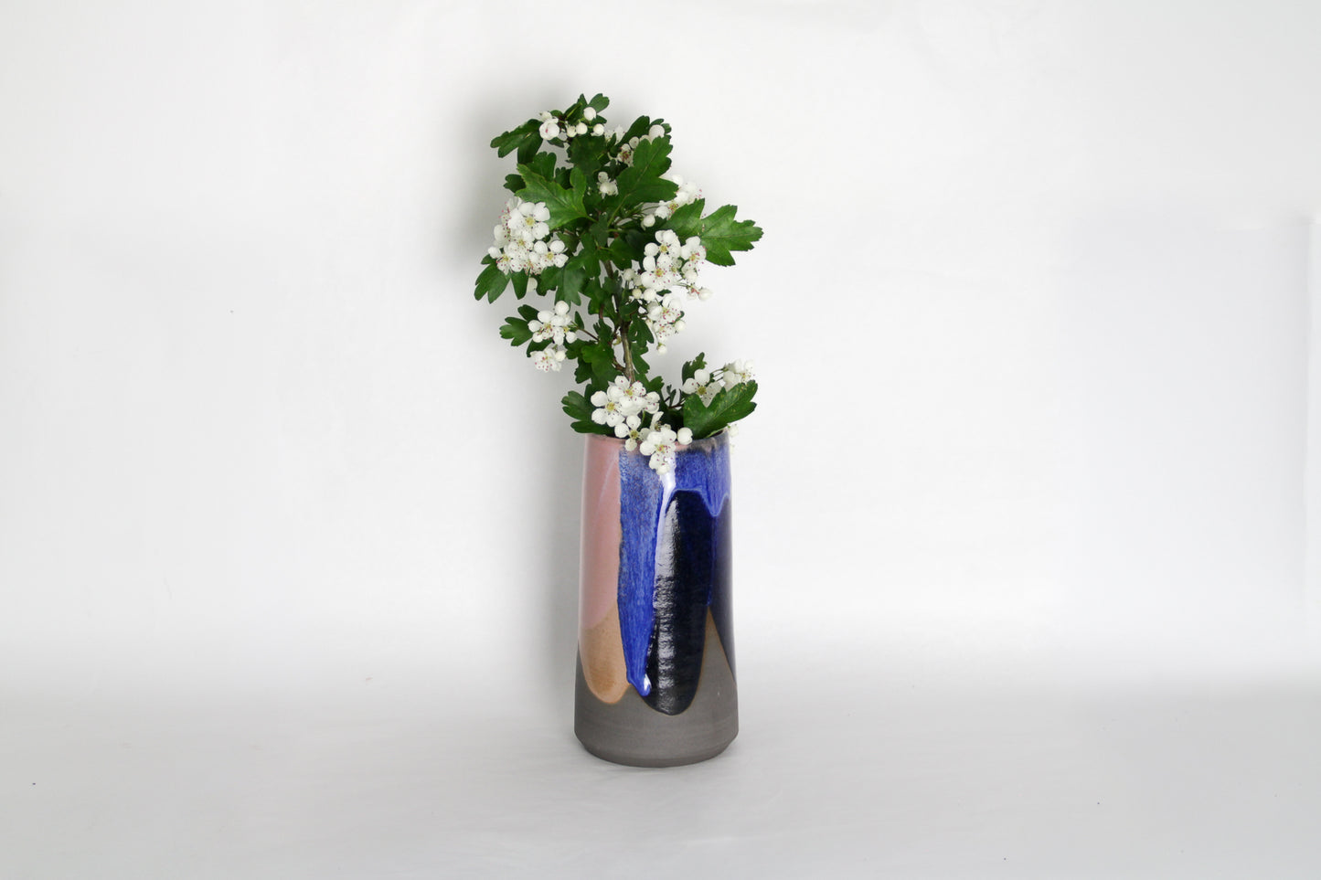 Image d'un grand vase en cérmique bleu et rose. Le vase contient des jolies fleurs blanches. Pièce artisanale décorative au style moderne.