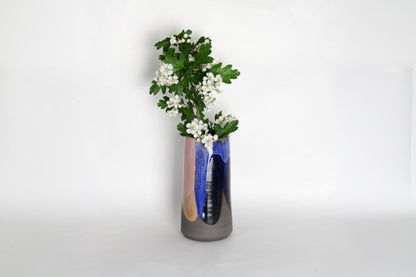 Image d'un grand vase en cérmique bleu et rose. Le vase contient des jolies fleurs blanches. Pièce artisanale décorative au style moderne.