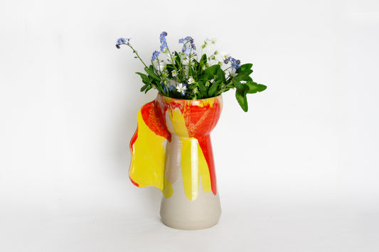 Image d'un vase en céramique aux couleurs jaune et rouge. Sa forme de coupe est originale. Le vase contient des fleurs.