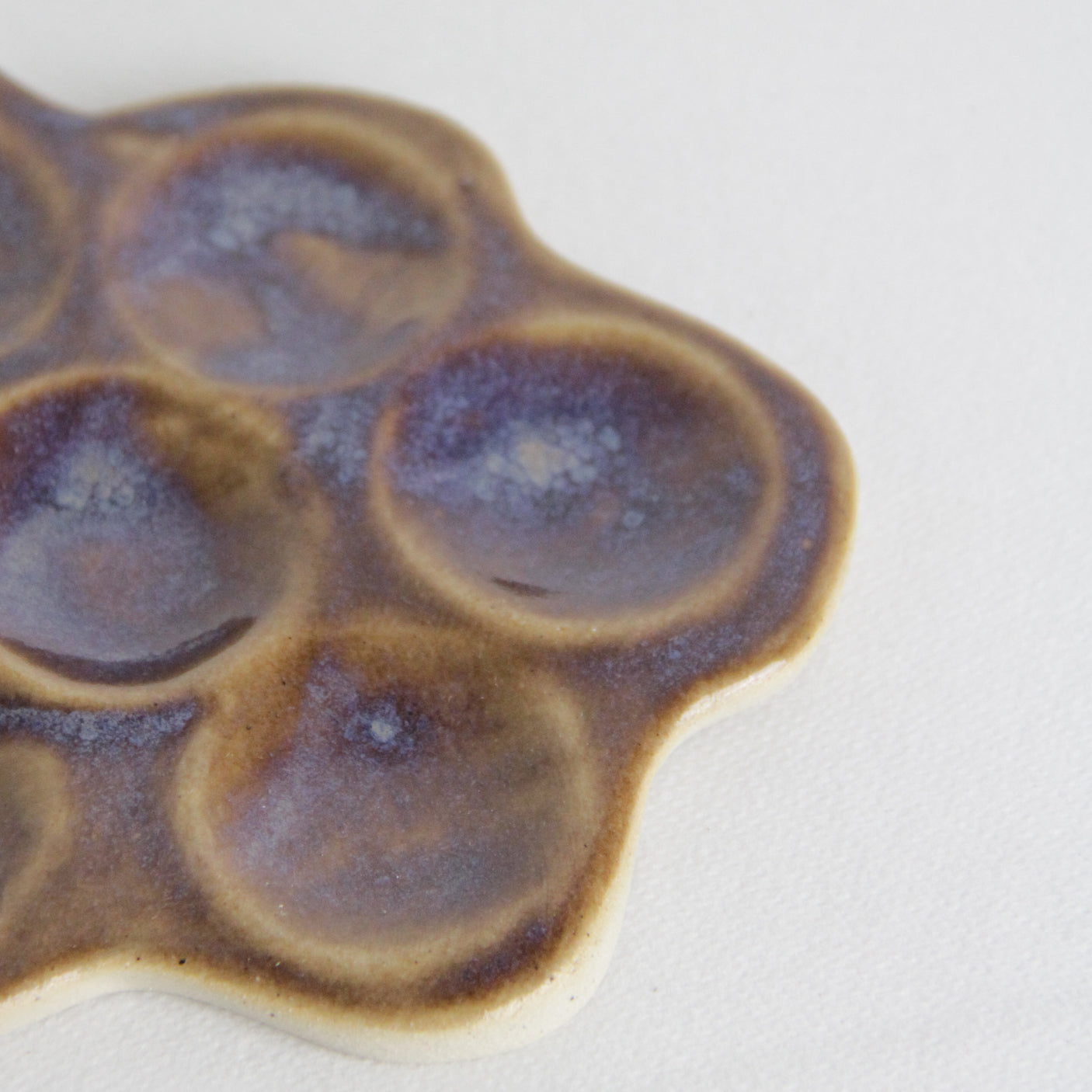 Zoom sur un détail de la marguerite en céramique de couleur violette. On observe les jeux de l'émail.