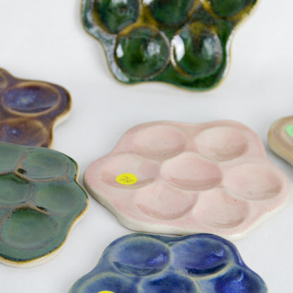 Image d'une composition de plusieurs objets plats en céramique en forme de marguerite, issus d'une fabrication artisanale.