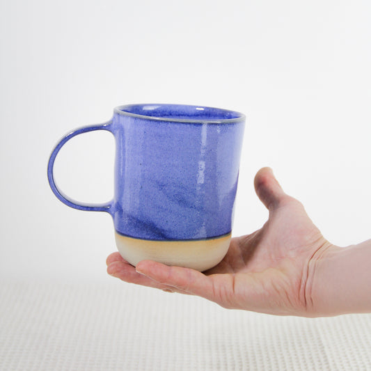 Image d'une main qui tient un grand mug bleu de 500 ml. L'anse est large et la couleur bleue est profonde et éclatante.
