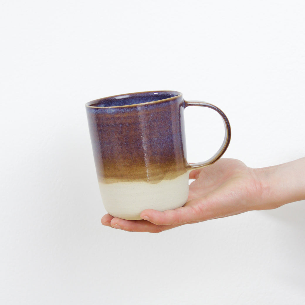 Image d'une main qui présente un mug en céramique artisanale