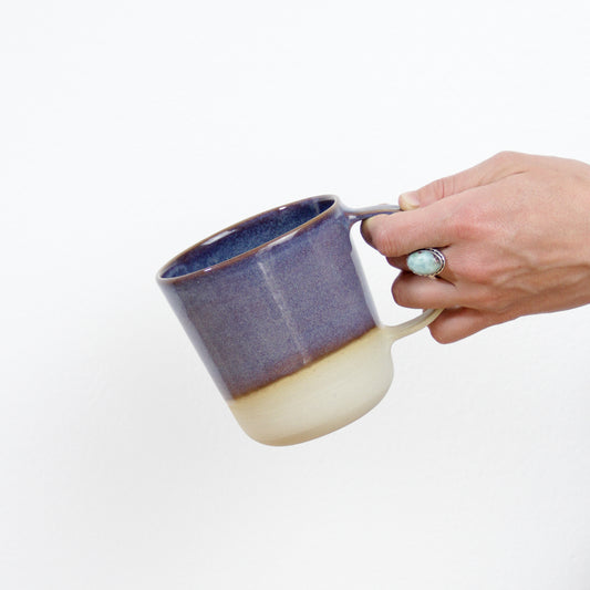 Image d'une main qui présente un joli mug violet nébuleux en céramique artisanale