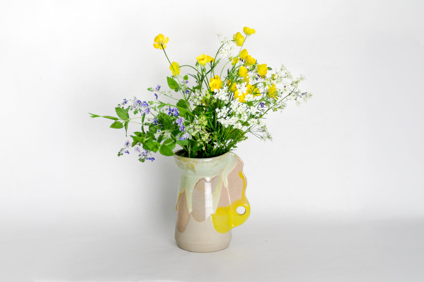 Image d'un petit vase en céramique aux couleurs vives. Le vase contient un joli bouquet de fleurs des champs.