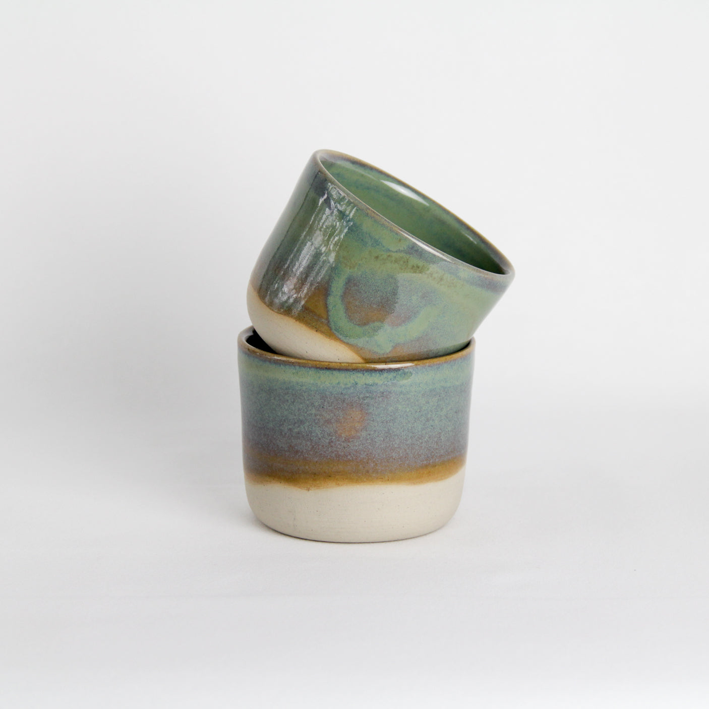 Image de deux petites tasses vertes qui s'empilent. Ce sont des pièces en céramique artisanale. 