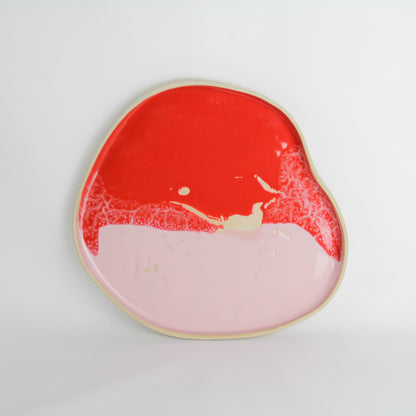 Image d'un plateau artisanal en céramique rose et rouge. Sa forme est aléatoire. Il mesure environ 27 cm de diamètre.