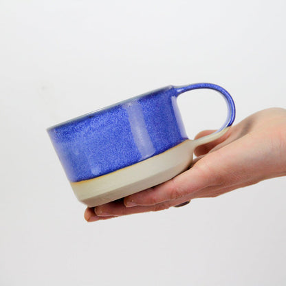 Image d'une main qui tient une petite tasse bleue en grès. Les nuances du bleu sont prononcées, la tasse est solide pour une utilisation quotidienne.