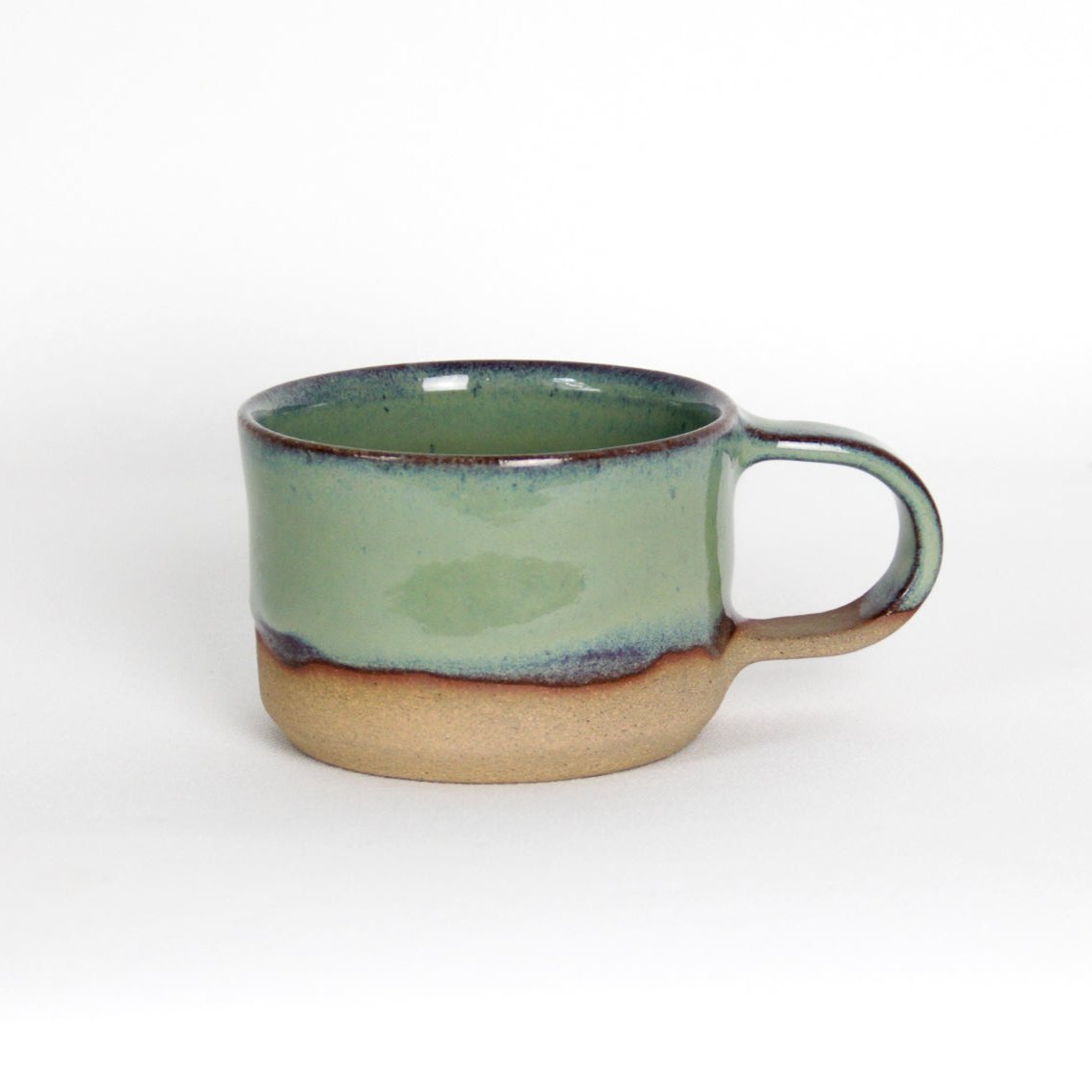 Image d'une petite tasse en grès de couleur verte. La tasse a un style moderne et coloré. L'émail est vert et une partie de la terre est visible pour un effet bi-matière original.