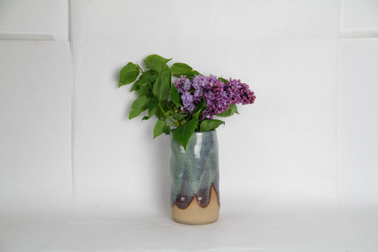 Image d'un vase en céramique avec du relief qui contient un bouquet d'hortensia. Le vase est vert. Une partie de la terre est visible ce qui créer un visuel intéressant.