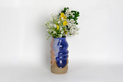 Image d'un vase en grès bleu et rose avec une bouquet de fleurs. Le vase a une forme irrégulière et élégante. C'est une pièce en céramique artisanale unique. 