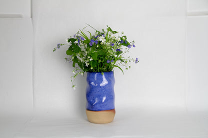 Image d'un vase bleu avec un bouquet de fleurs des champs. Le vase en céramique est irrégulier. On distingue la terre sur le bas du vase ce qui lui apporte une esthétique moderne.