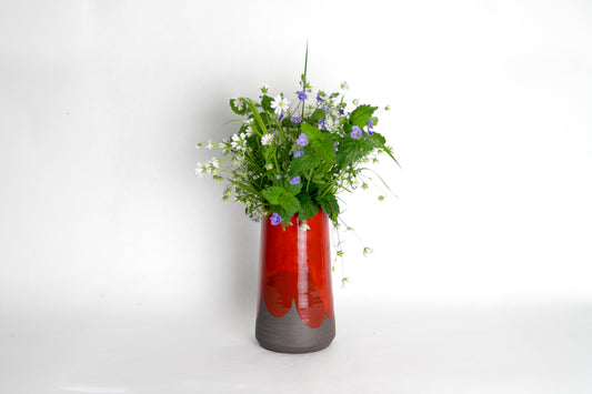 Image d'un vase en céramique avec une bouquet de fleur. Le vase a une forme de cône, il est émaillé en rouge sur un grès anthracite. Il est bien contrasté.