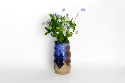 Image d'un vase en céramique avec un bouquet de fleur. Le vase a une forme irrégulière. Il est bleu et marron.