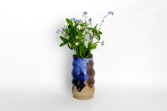 Image d'un vase en céramique avec un bouquet de fleur. Le vase a une forme irrégulière. Il est bleu et marron.